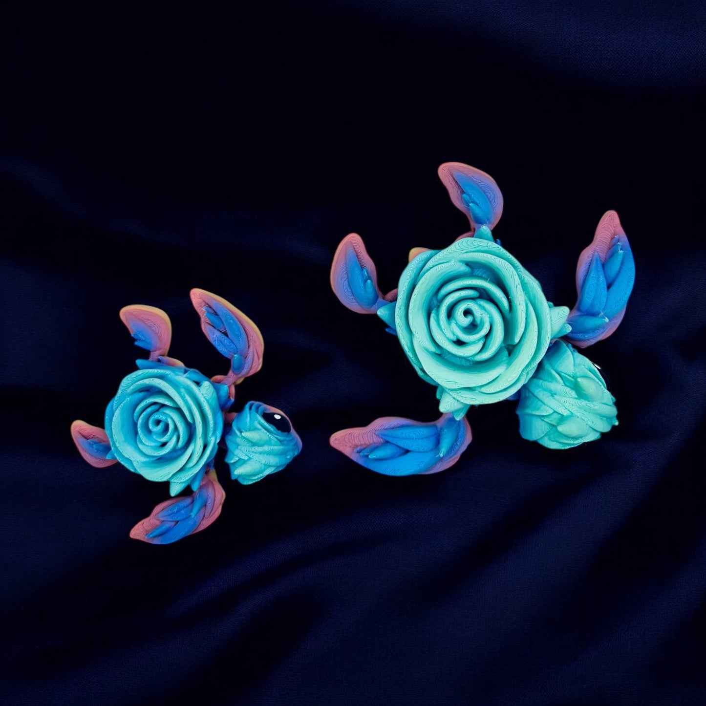 Two multi colored turtles with a rose as their shells - taken from the top view on a black background.