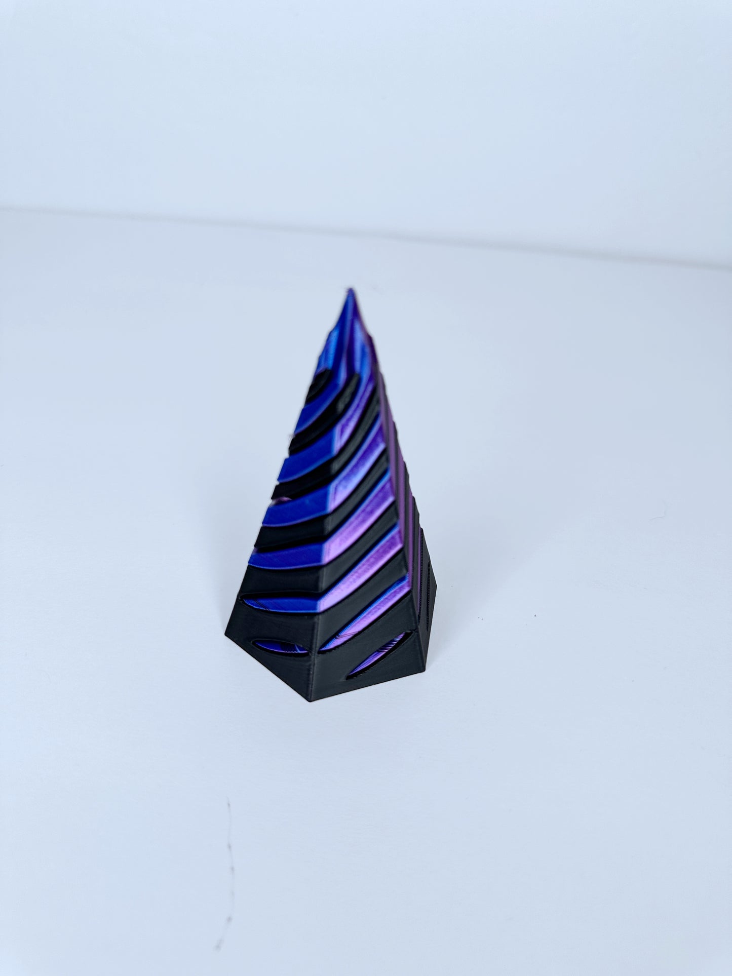 3d printed cone shaped fidget in black and blue/purple on a white surface and white background.