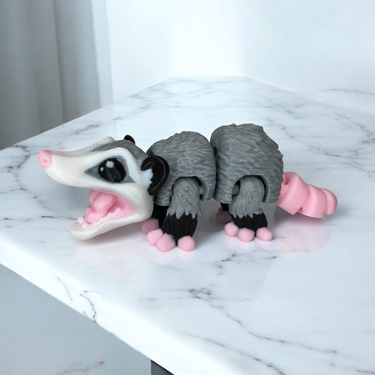 3D printed baby opossum figure with gray body and pink accents on its face and feet, against a white background.