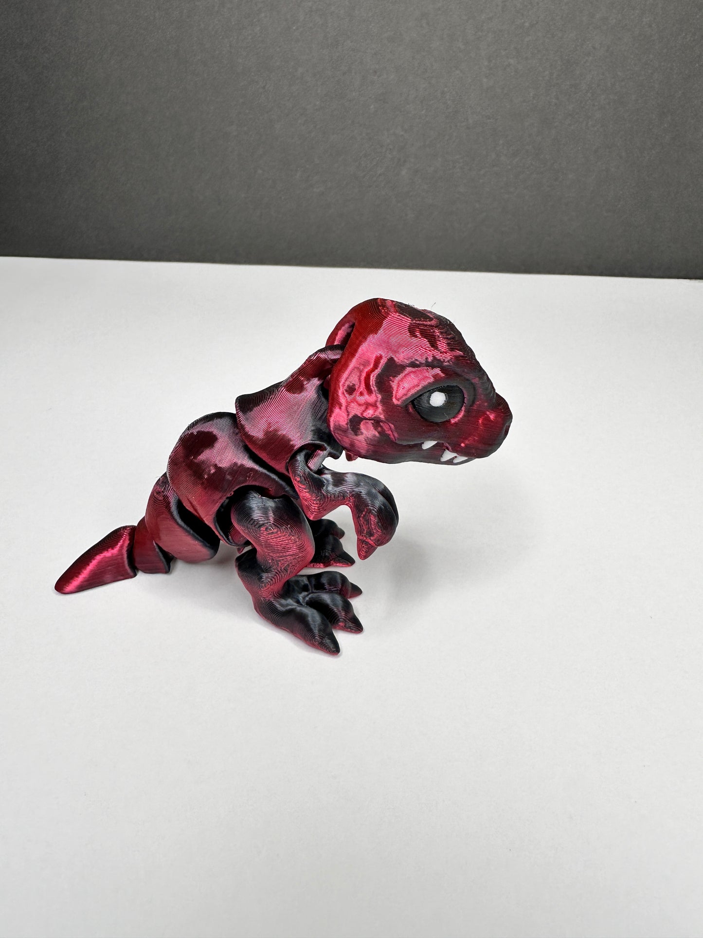 A 3d printed red/black t rex dinosaur standing on a white surface against a black background.