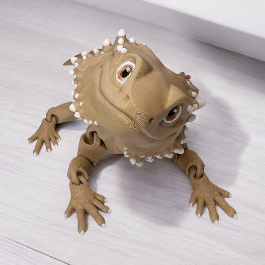 A 3d printed bearded dragon posed on a wooden surface.