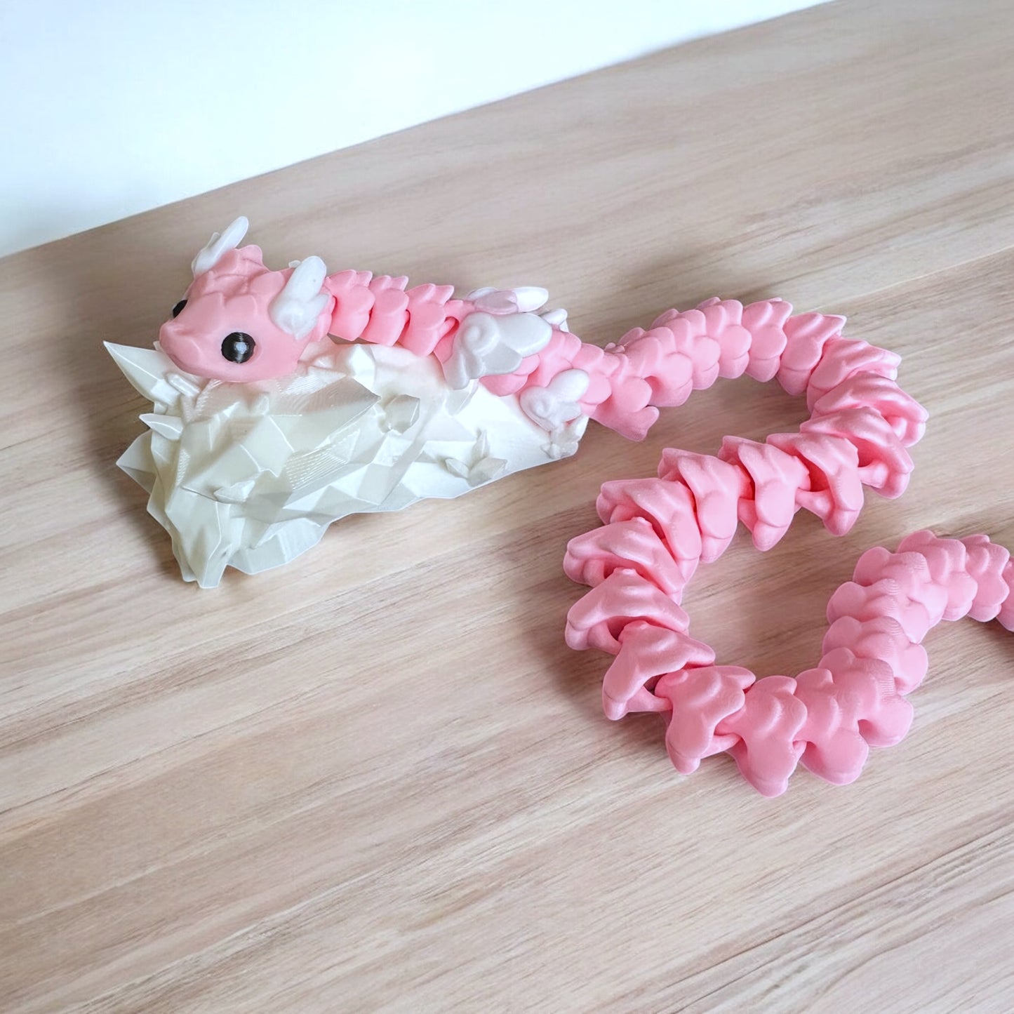 Pink 3d printed snake on top of a white rock on a wood surface.