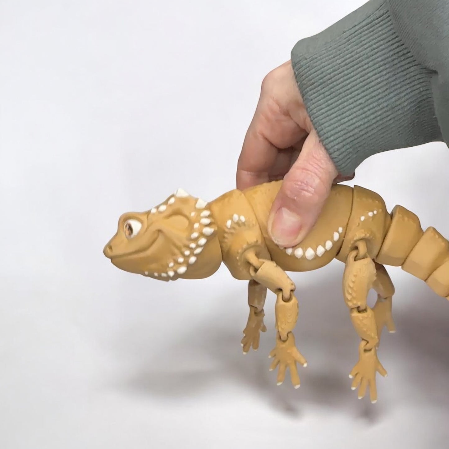 A hand holding a 3d printed bearded dragon against a white background.