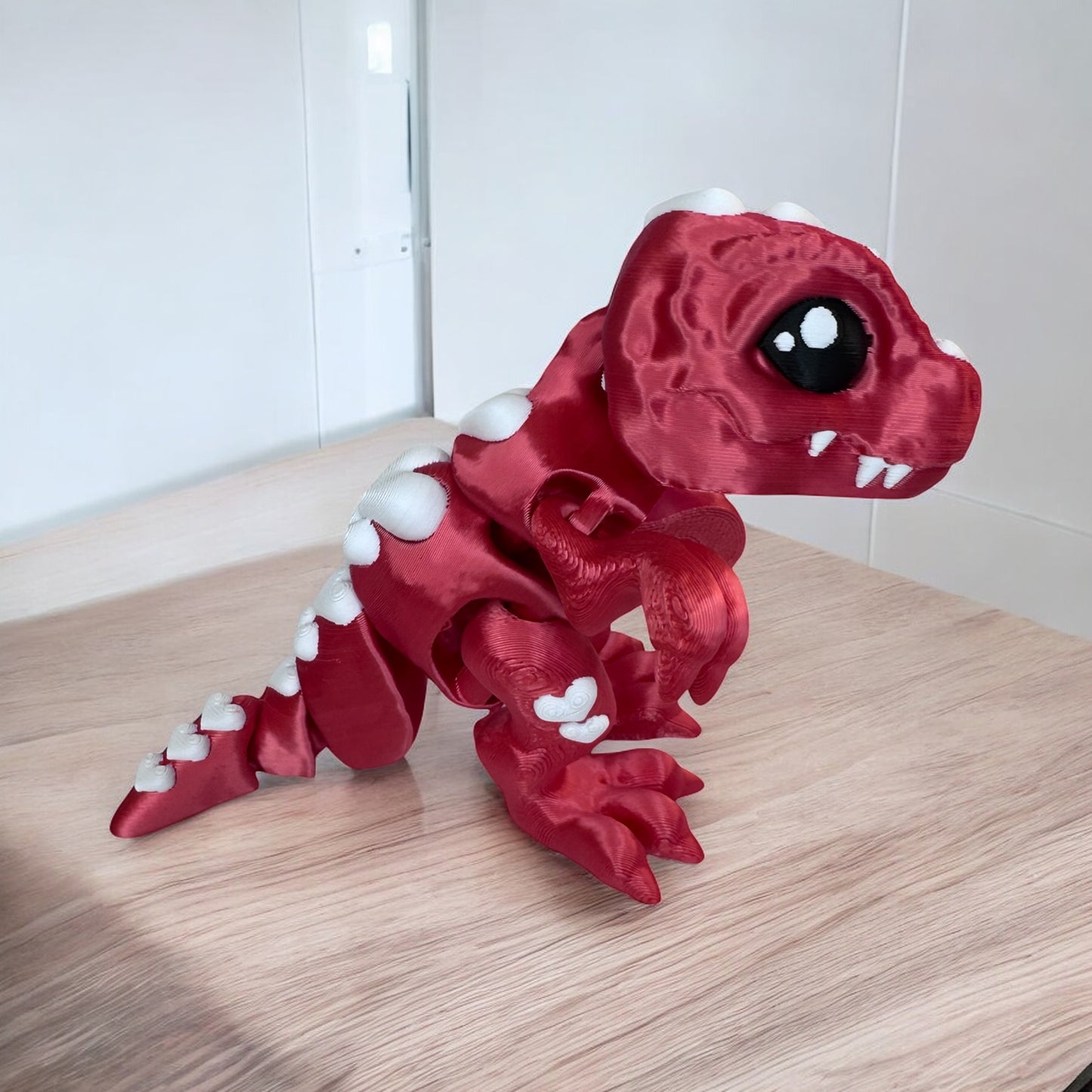 3d printed t rex figurine in red with white hearts down it's back, standing on a light wood surface