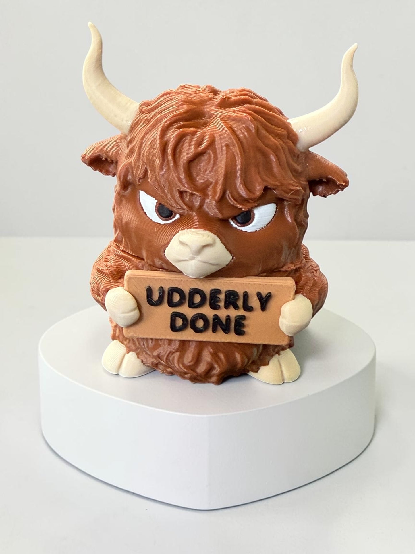 3d printed highland cow holding a sign that says "Udderly done"