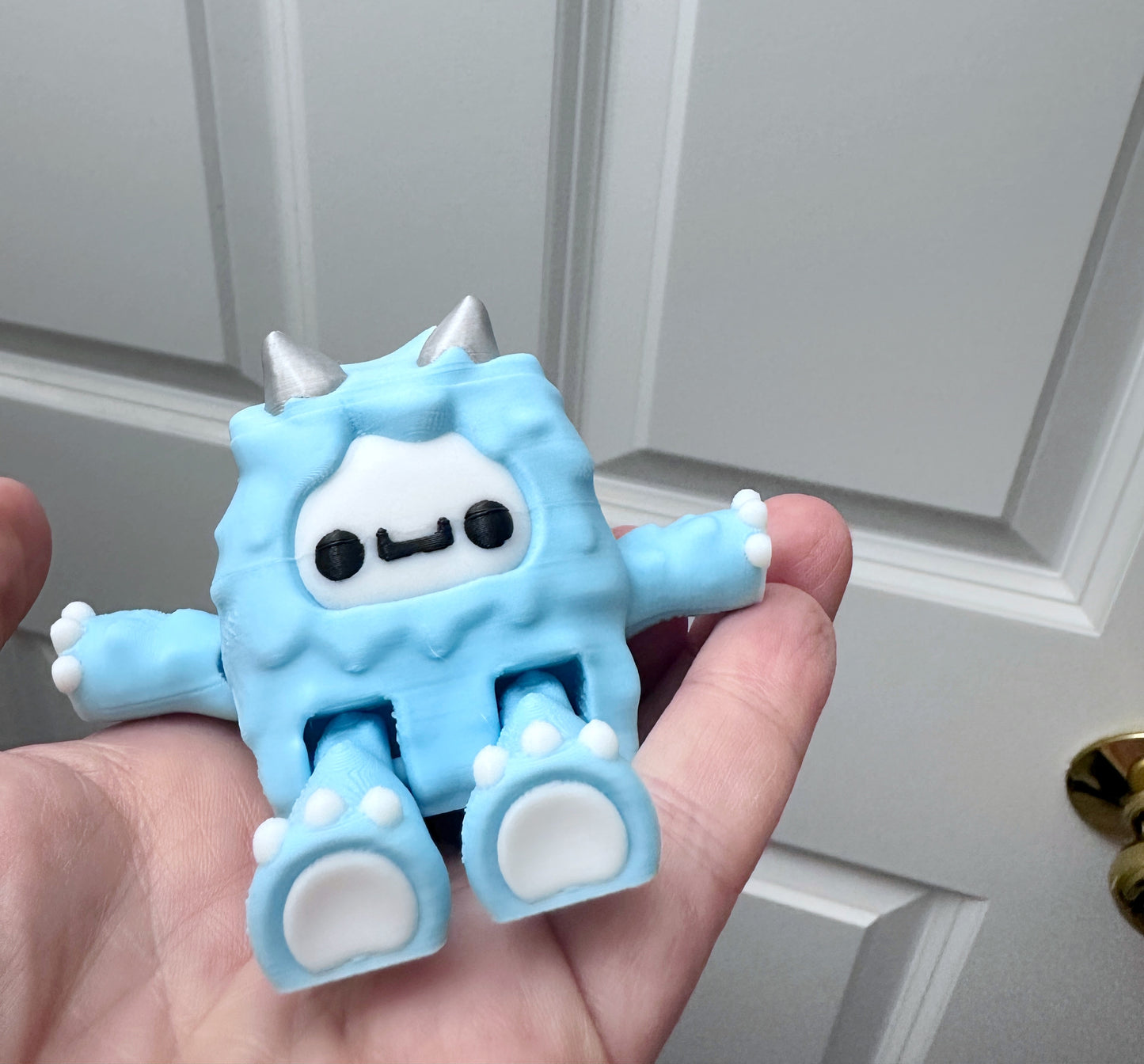 Hand holding a light blue 3d printed yeti figurine against a white background.