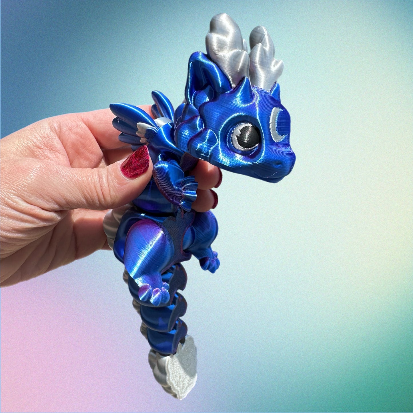 Blue and silver 3D printed dragon held in a hand against a gradient background