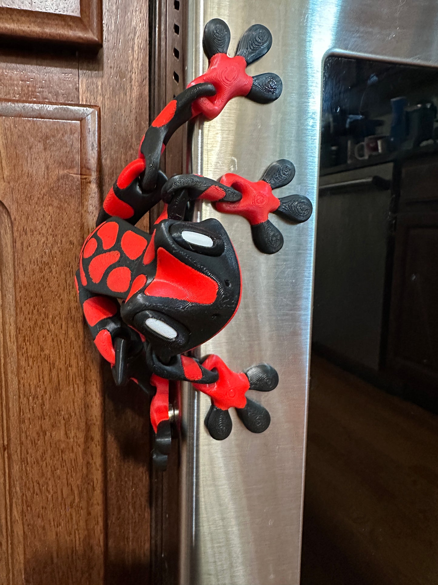 Red and black 3d printed frog hanging onto a metallic surface