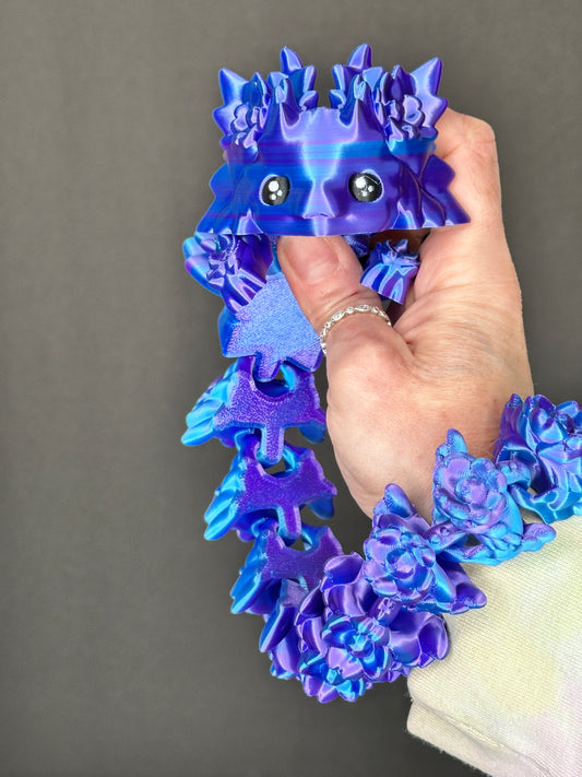Hand holding a shiny blue and purple 3d printed axolotl dragon. Light black background.