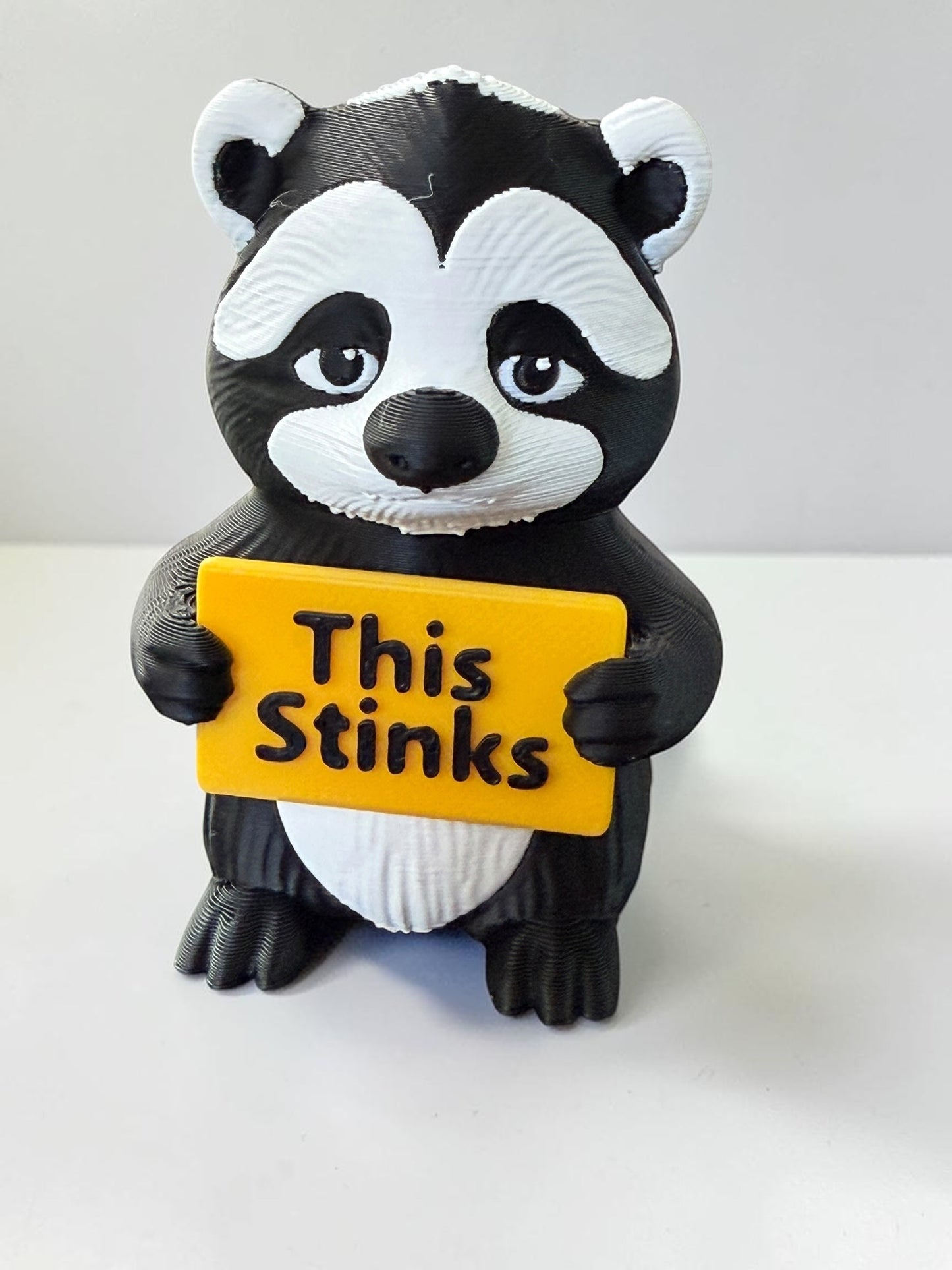 3d printed skunk holding a sign that says 'This Stinks"
