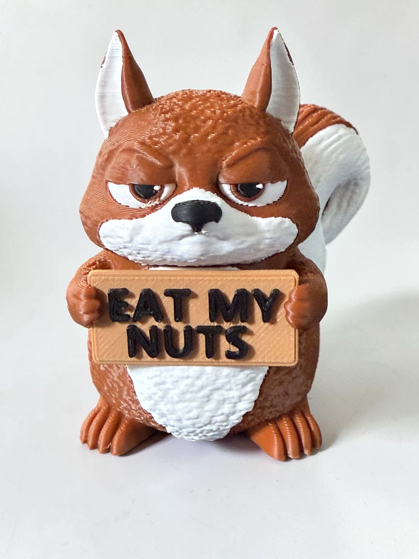 3d printed squirrel holding a sign that says "Eat my nuts"