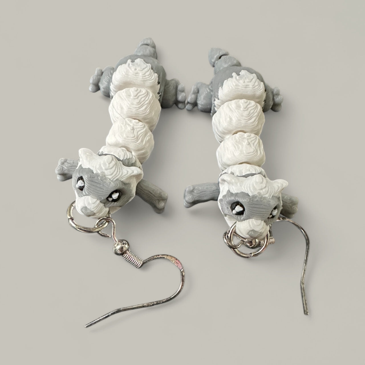 Pair of gray and white ferret shaped earrings on a light gray background