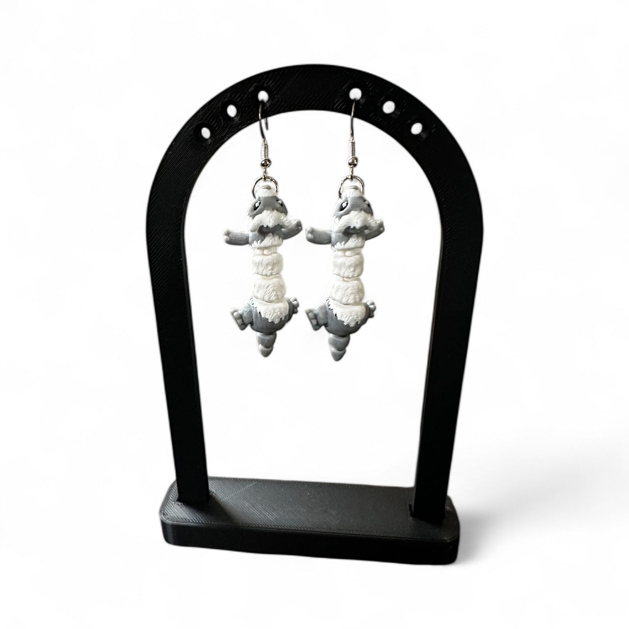 Pair of ferret-shaped earrings on a black stand against a white background