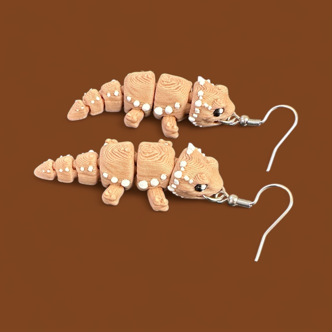 Bearded dragon shaped earrings on a brown background