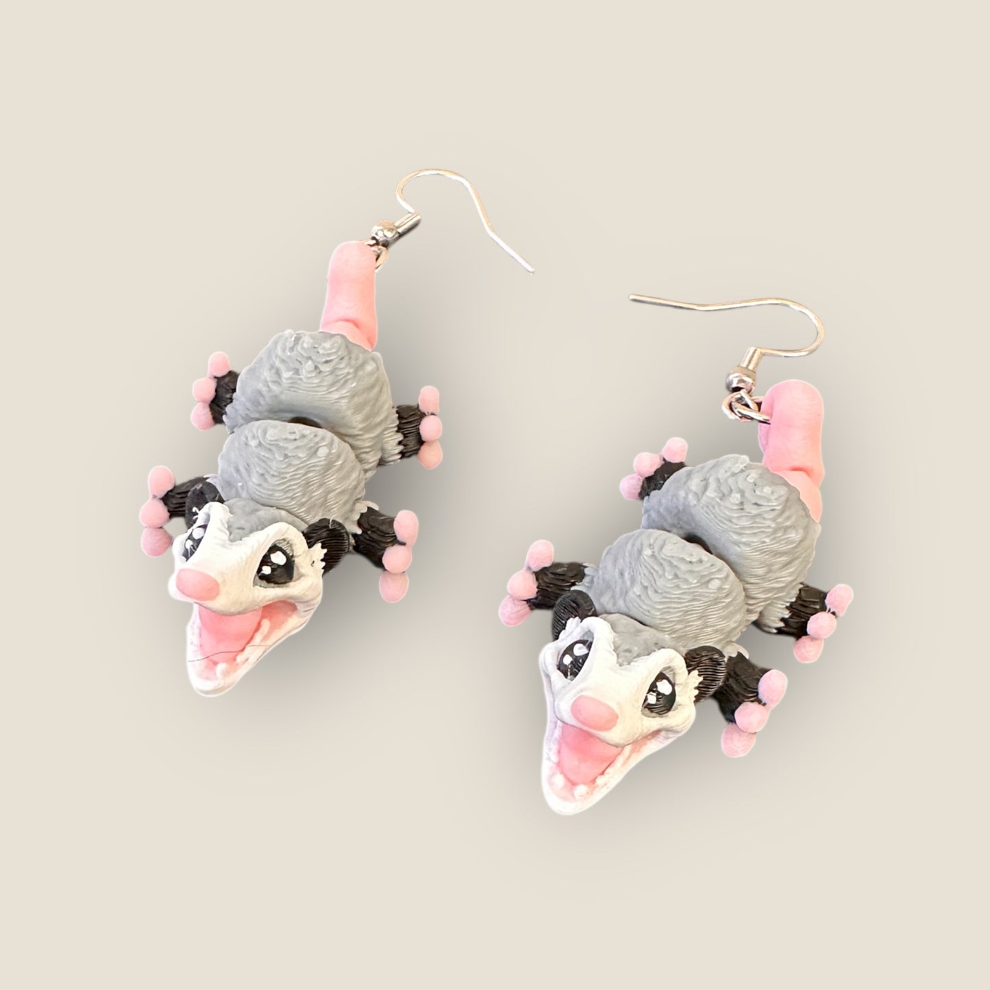 Pair of earrings shaped like cartoon-style opossums on a light gray background