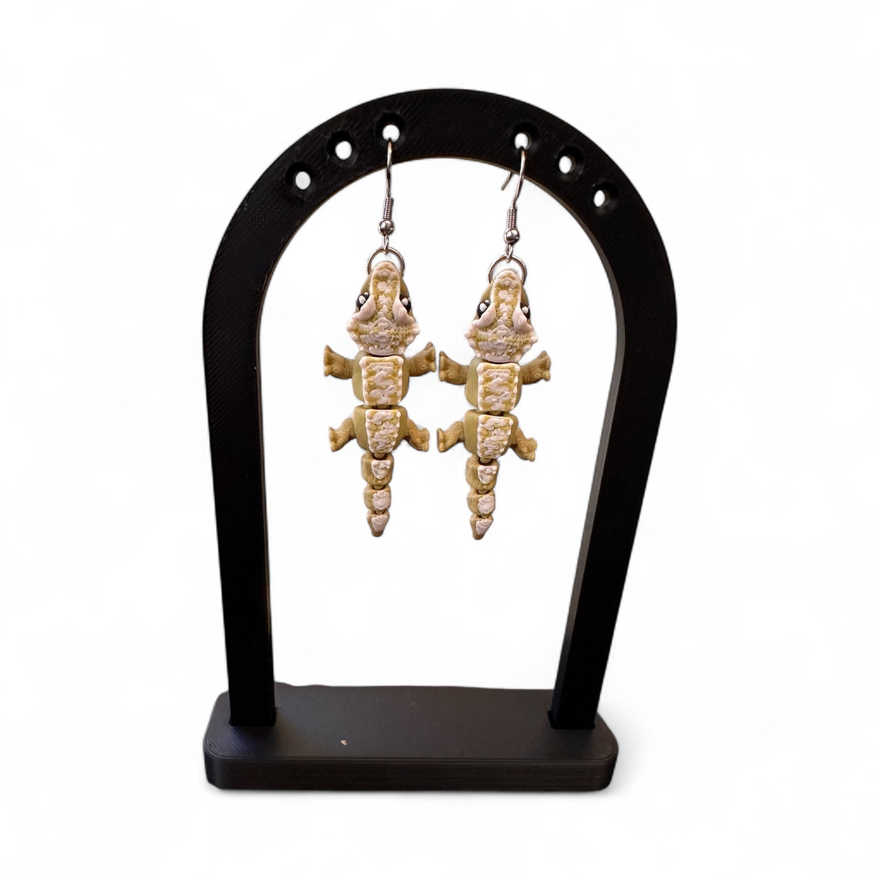 Pair of gecko-shaped earrings on a black stand against a white background