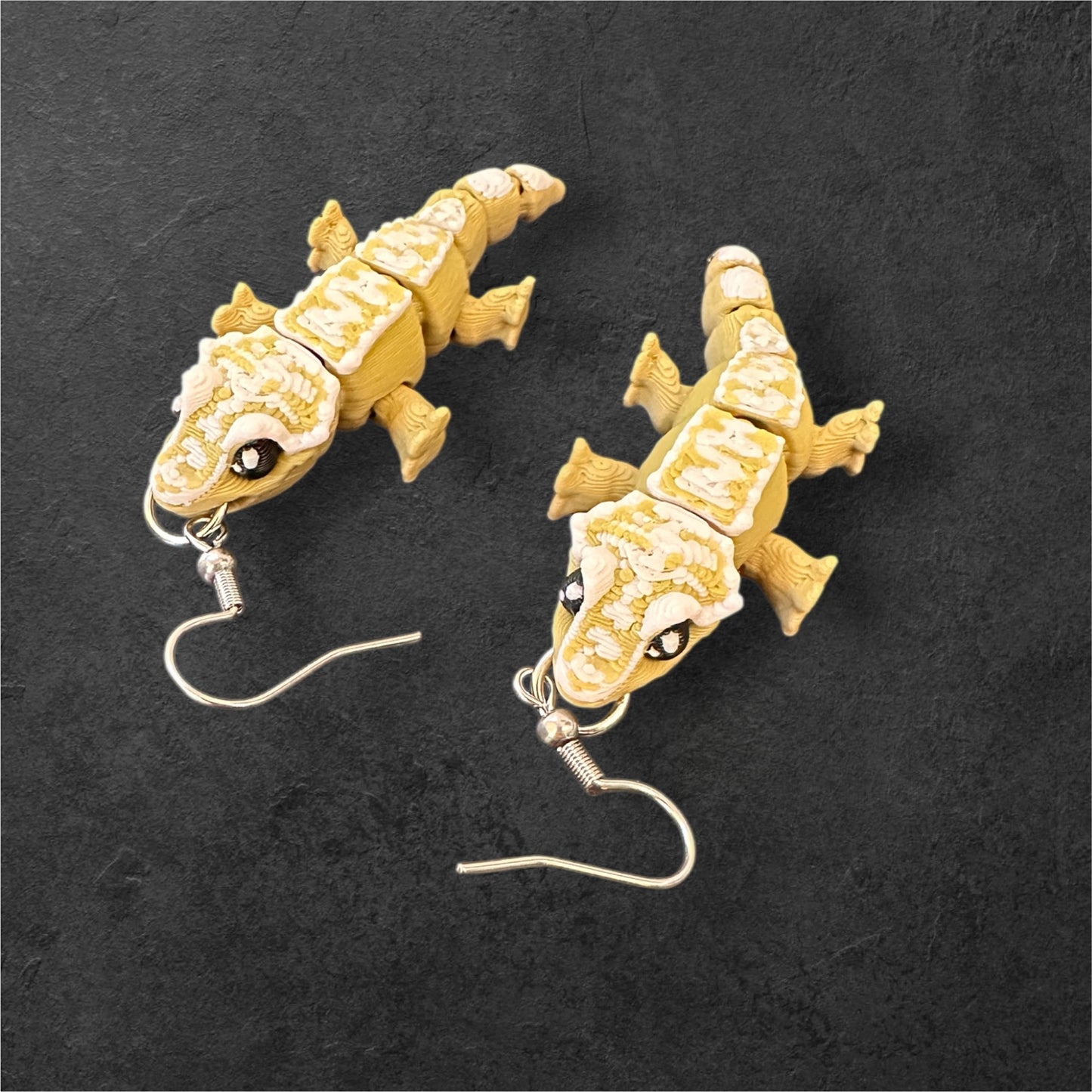 Pair of gecko-shaped earrings on a dark background