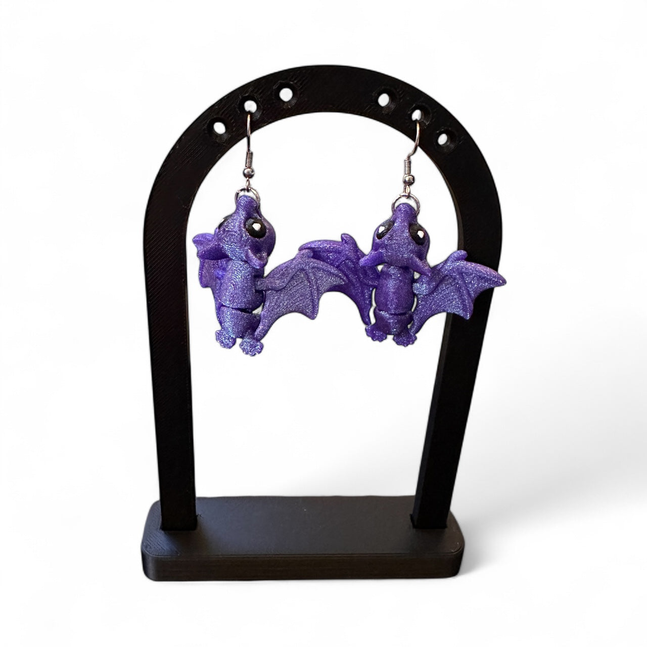 Purple bat-shaped earrings on a black stand against a white background