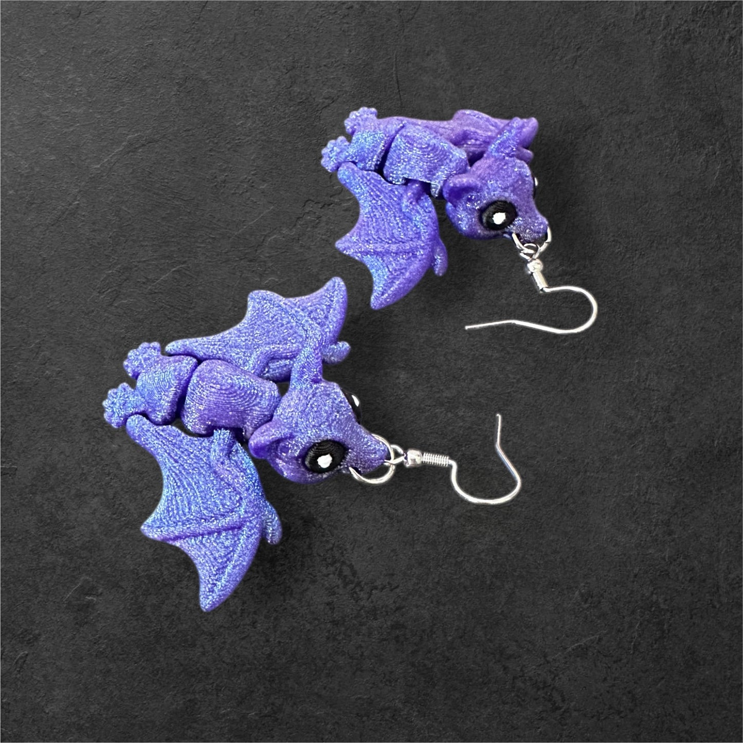 Pair of purple bat-shaped earrings on a dark background