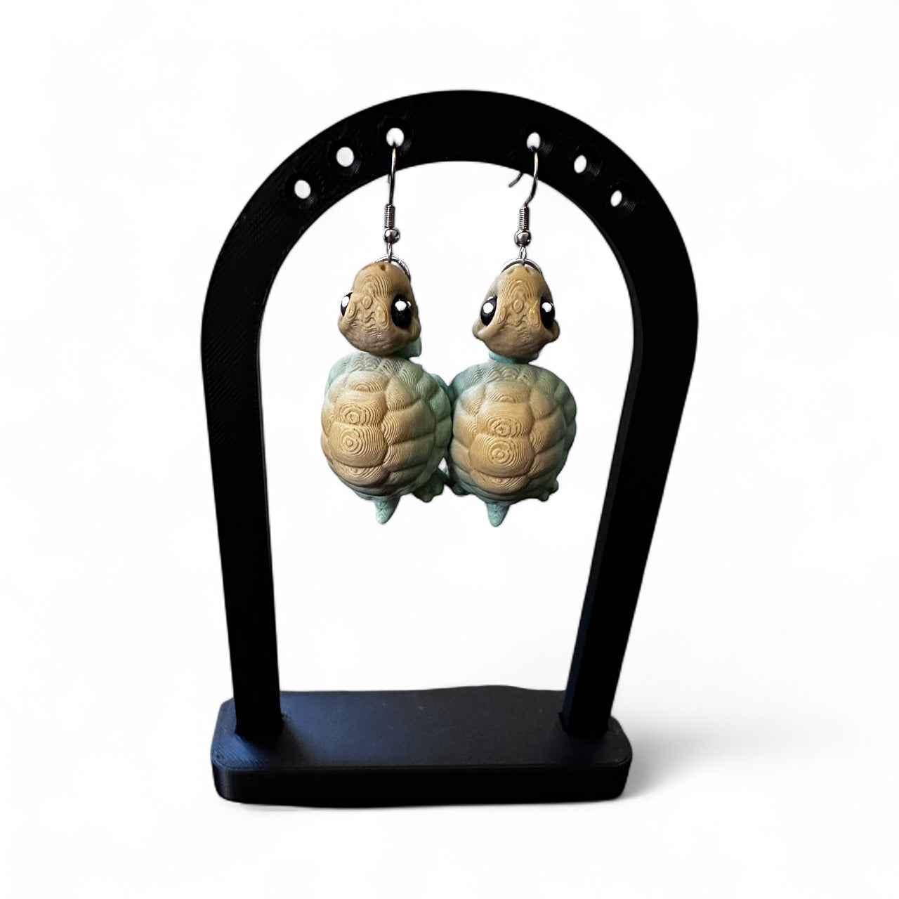 Tortoise-shaped earrings on a black stand against a white background